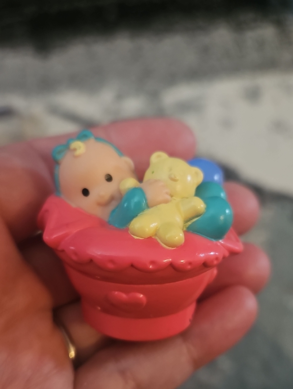 Fisher-Price Little People baby figure holding a teddy bear in a pink seat,